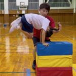 金沢市教室にて、跳び箱の台上前転に挑戦する女児の子供と補助をする大久保先生