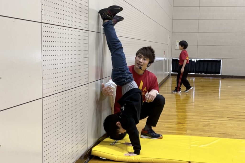 小松市教室にて、補助倒立をする男児の子供と、指導する大久保先生