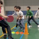 白山市教室にて、オリジナルの「かべ鬼ごっこ」をする万遍の笑顔の小学生の子供四人と、追いかける大久保先生