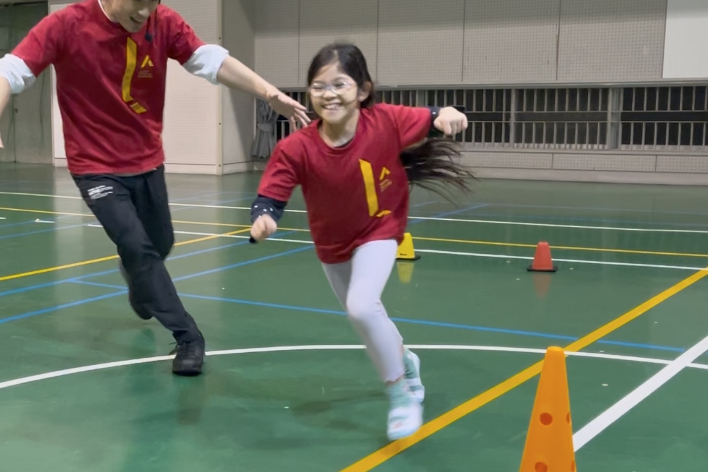 白山市教室にて、楽しそうに走り抜ける笑顔の小学生の子供と、追いかける大久保先生