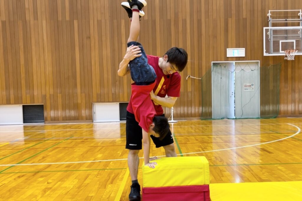金沢市、額谷教室にて、跳び箱二段の倒立台上前転に挑戦する小学生の子供と、補助をする大久保先生