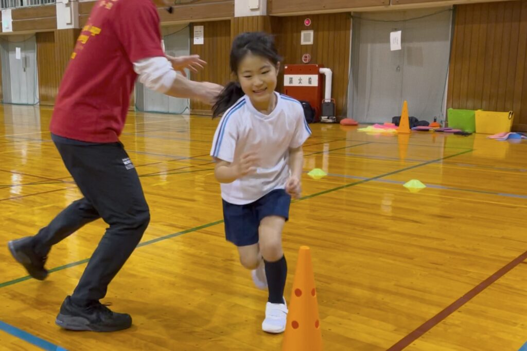 金沢市冨樫教室にて、楽しそうにかけっこをする笑顔の小学生の女児の子供と指導する大久保先生