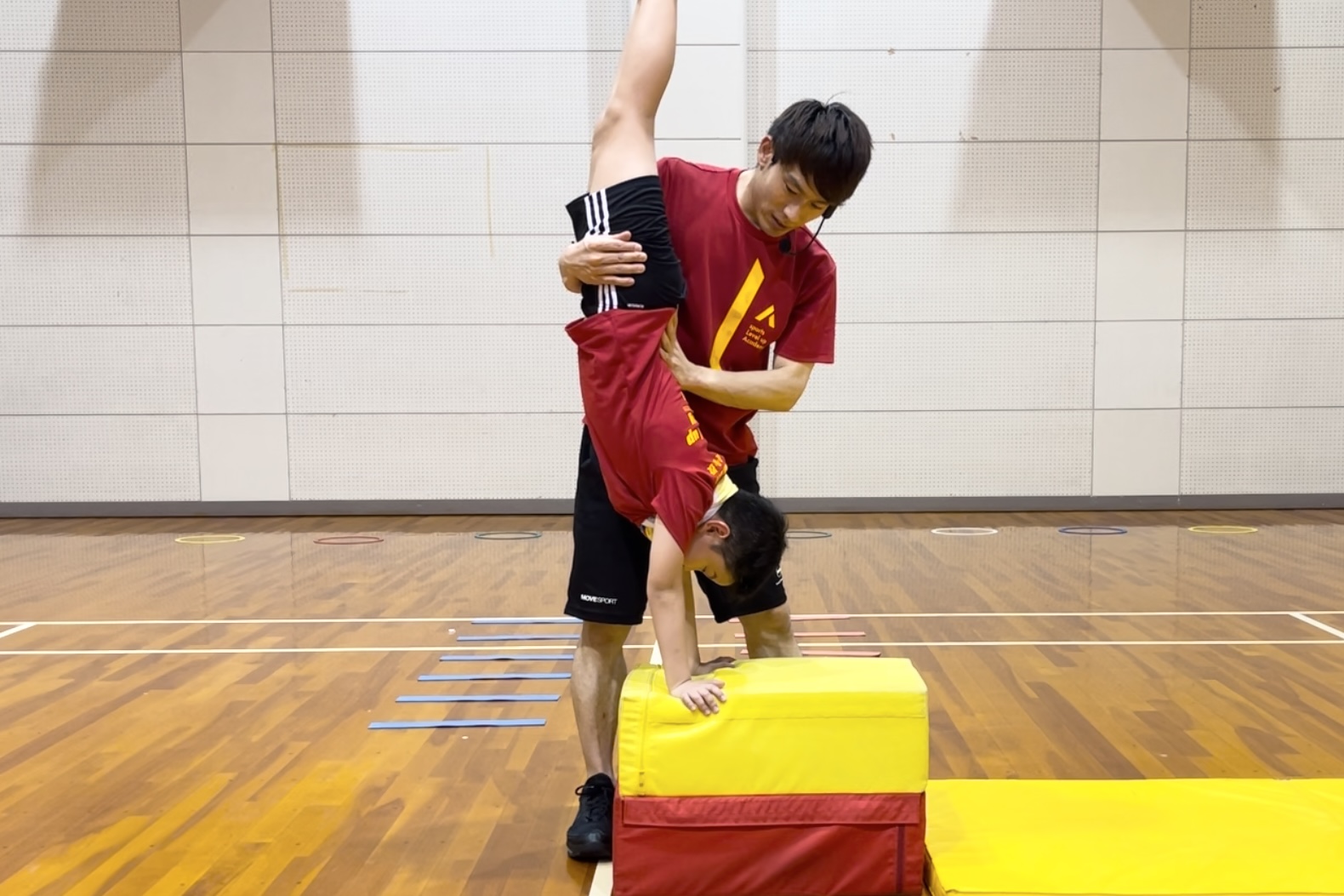 加賀市教室にて、跳び箱の倒立台上前転で、跳び箱の上で逆立ちをする小学生男児の子供と、補助をする大久保先生