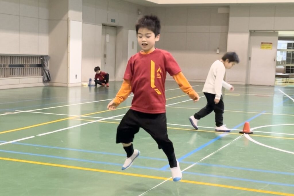 白山市の体操教室「大久保先生のスポーツレベルアップアカデミー白山市会場」にて、オリジナルの運動神経トレーニング「ゴムひもリズムジャンプ」をする小学生男児の子供
