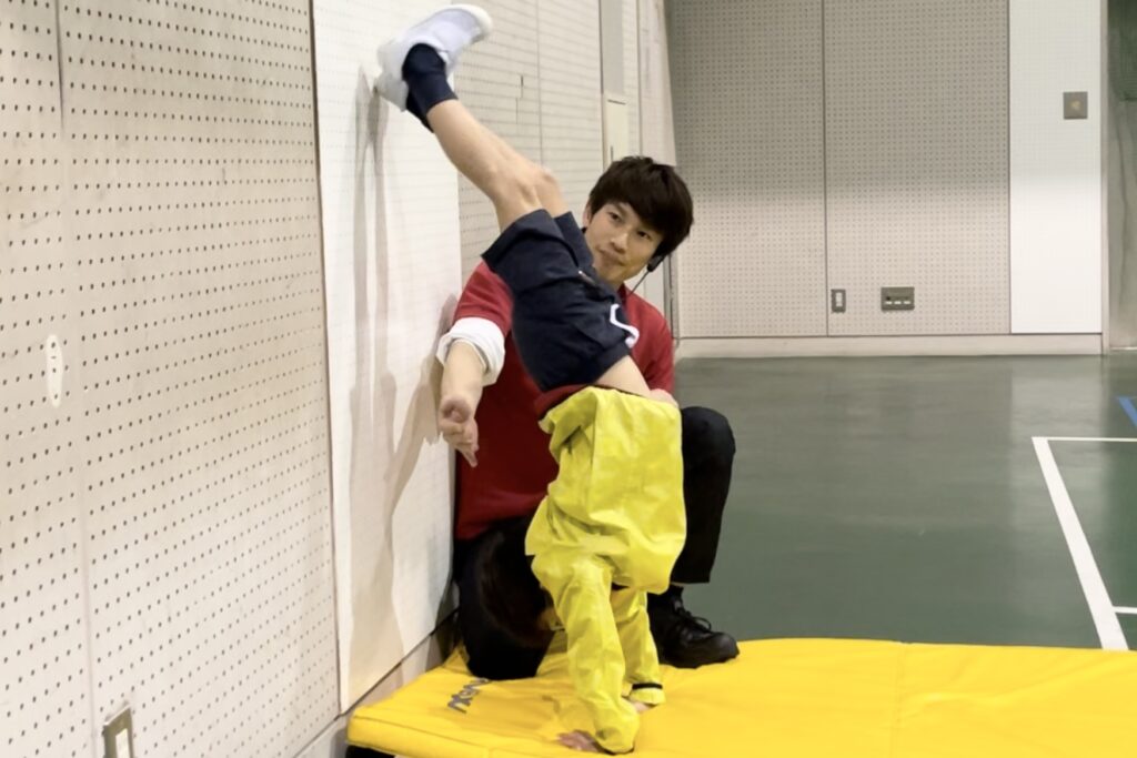 白山市教室にて、かべ倒立をかっこよく行う小学生男児の子供と、笑顔で見守る大久保先生