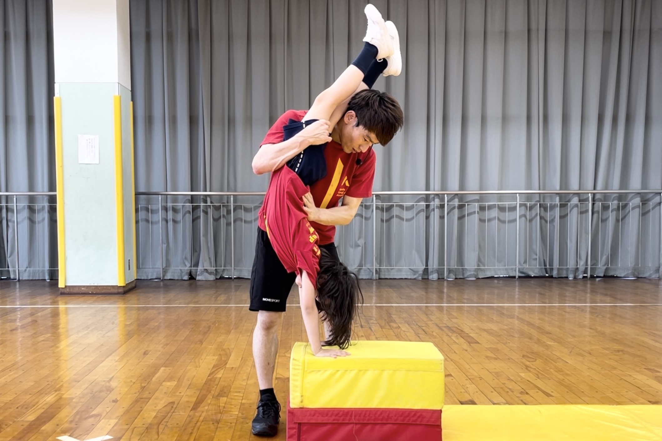 野々市教室にて、跳び箱の「倒立台上前転」に挑戦している小学生の子供と、その補助をする大久保先生