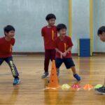 野々市市教室にて、オリジナルの「コーン壁鬼ごっこ」をする笑顔の子供三人