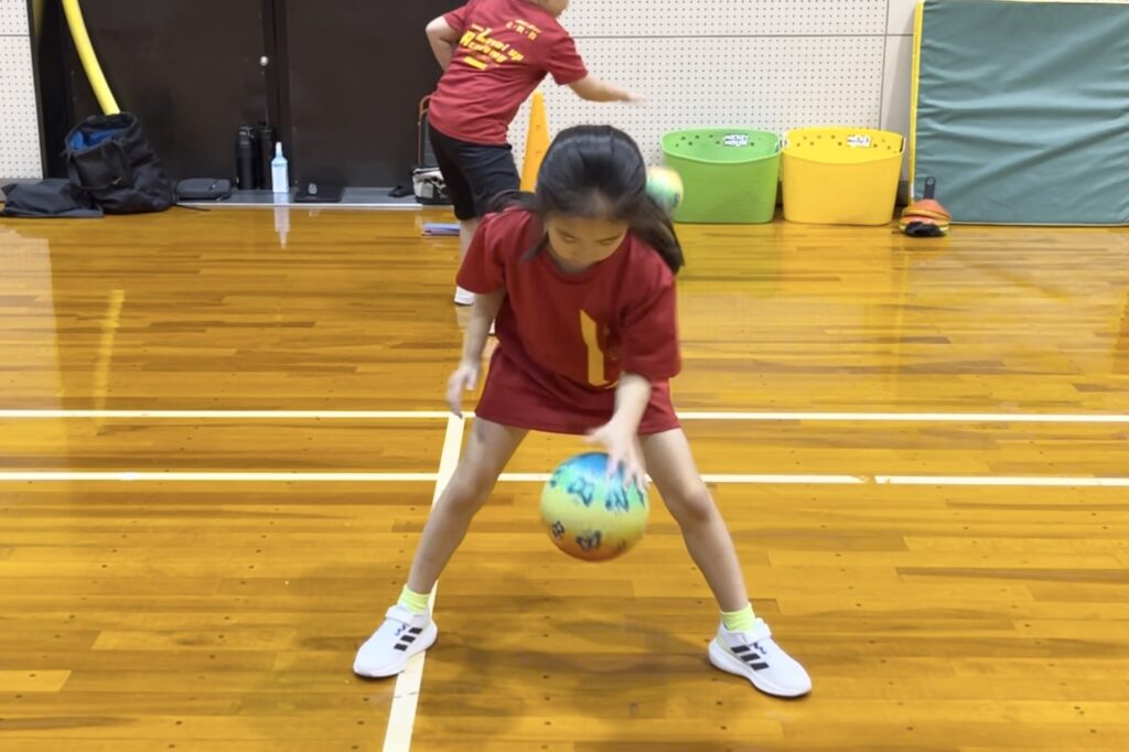 加賀市教室にて、ボールつきの「ドリブル」を一生懸命に練習する小学校低学年女児の子供