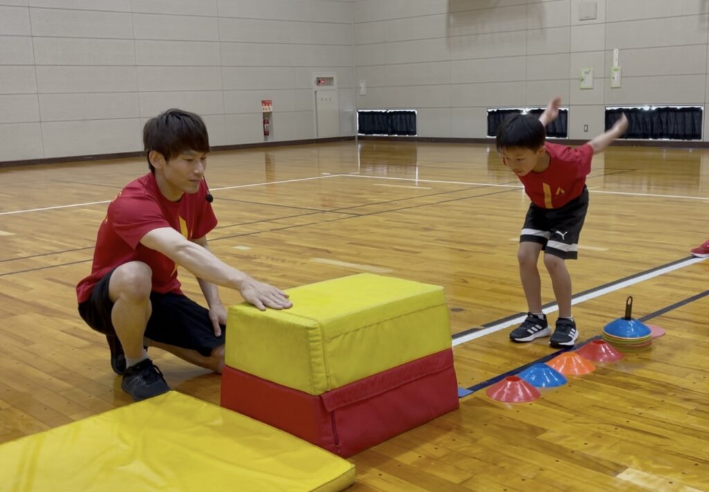 小松市の子ども体操教室で跳び箱を練習する様子。大久保先生が手本を示しながら、フォームとタイミングを丁寧に指導。