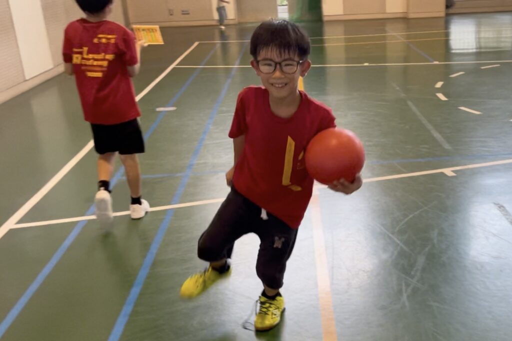 白山市教室にて、赤いボールを持って笑顔で走る男の子。体育館での運動中に楽しそうな様子を見せている。