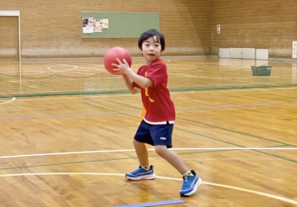 福井市の体操教室「大久保先生のスポーツレベルアップアカデミー福井市教室」にて、幼児がドッジボールを真剣な表情で投げるフォーム練習をする様子