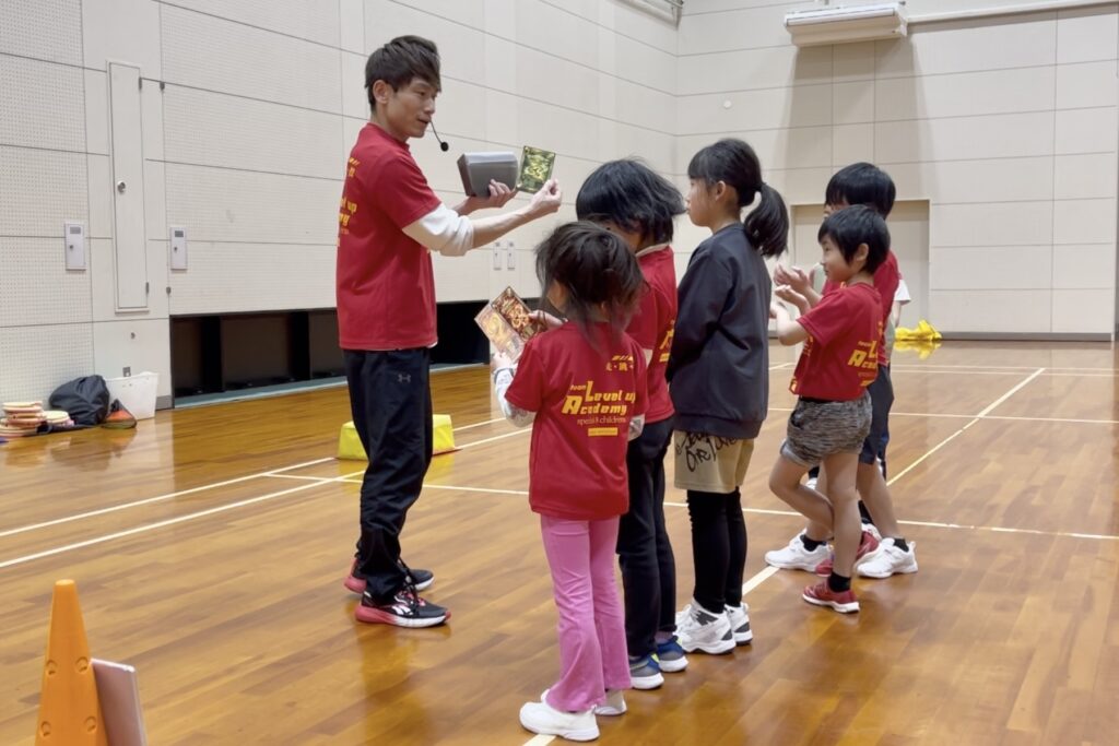 3ヶ月に一度の称号カード授与式で、大久保先生が子供たちにスキル認定の称号カードを渡している様子