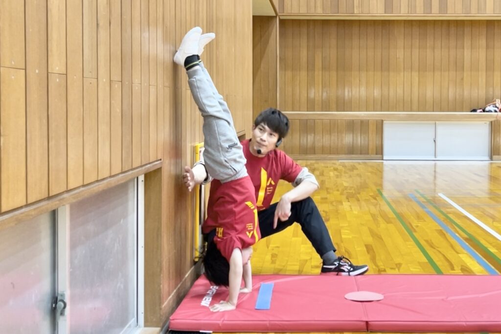 金沢市教室にて、きれいな形で壁倒立をする子供と、笑顔で補助姿勢をとる大久保先生