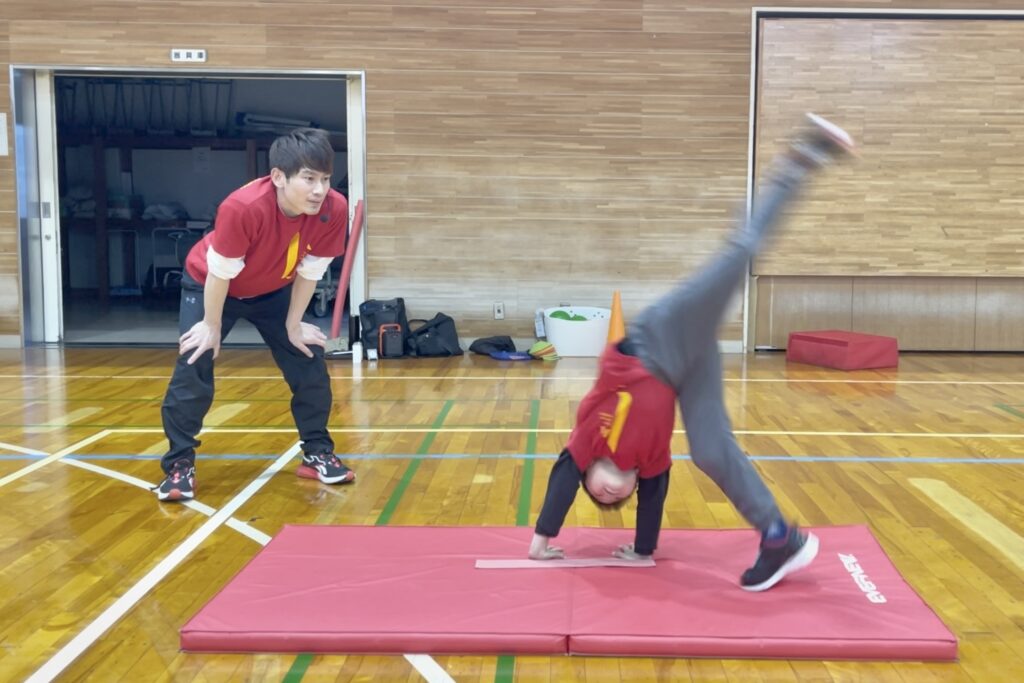 福井市教室にて、側転を練習する幼児と、その子を笑顔で見守る大久保先生