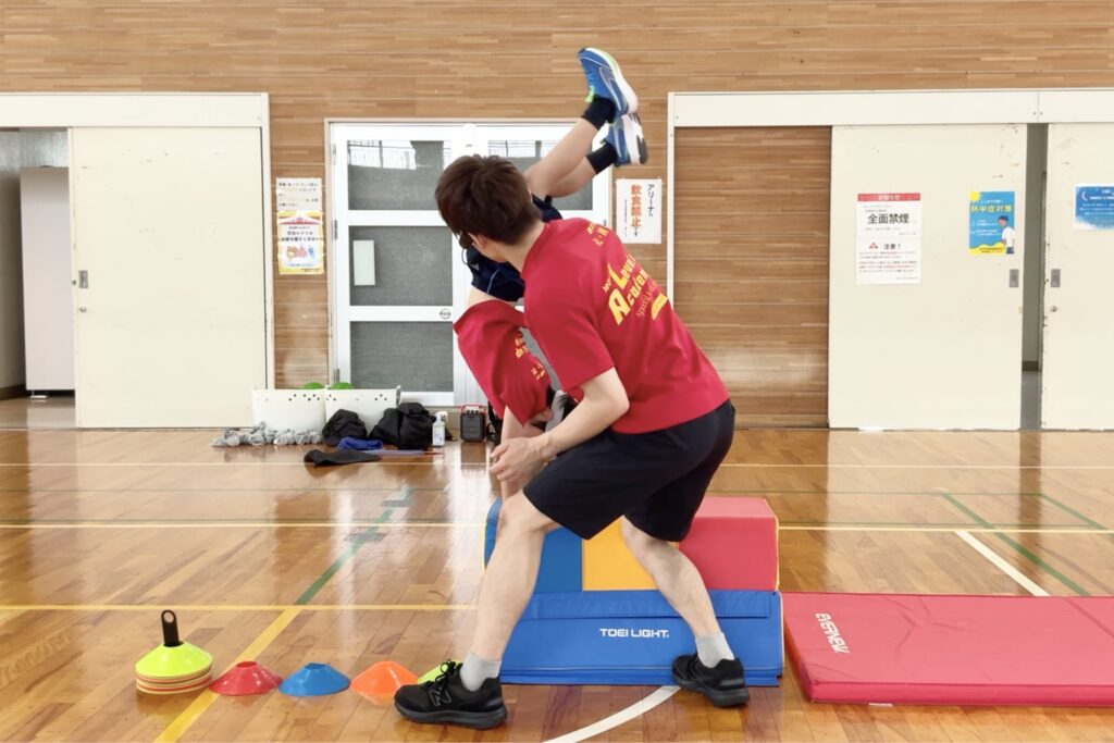 福井市北体育館にて、跳び箱の「台上倒立」にチャレンジする幼児と、補助をする大久保先生