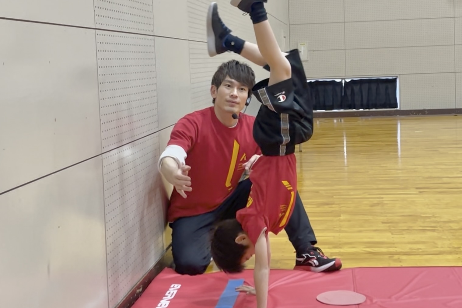 小松市教室の、体操競技のマット運動にて、倒立にチャレンジする子どもと、笑顔でサポート体制をとる大久保先生