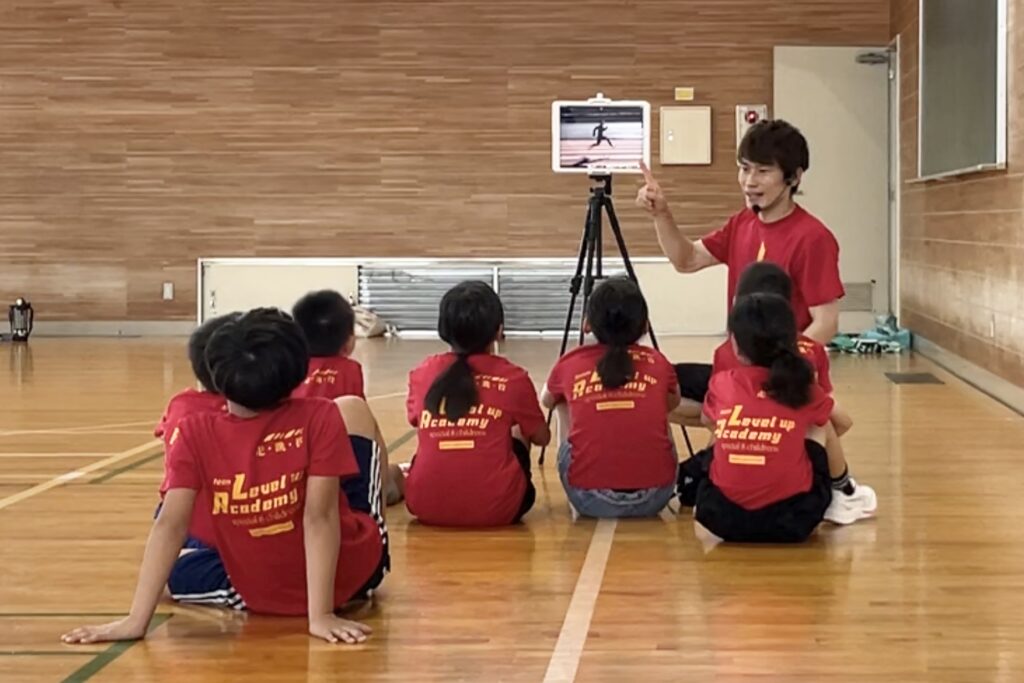 福井市教室にて、タブレットを使って子供達に動きのポイントを教える大久保先生と、その説明を聞く子供たち