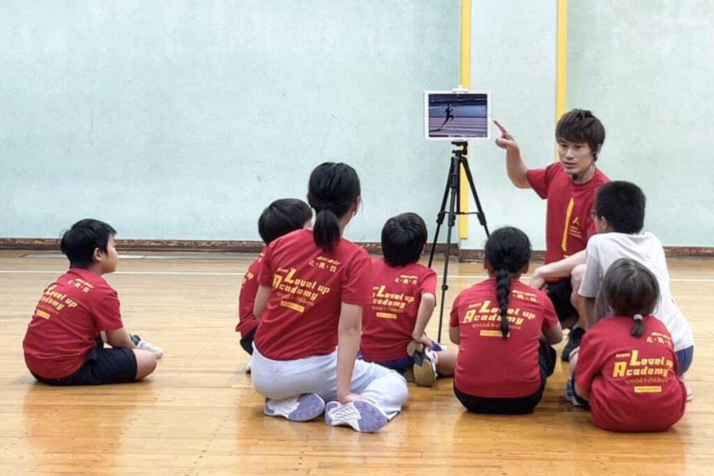 野々市教室にて、タブレットを用いて動きのポイントを説明する大久保先生と、その説明を聞く子供たち