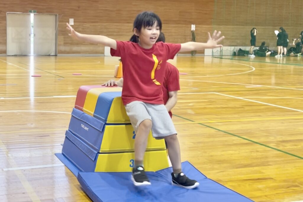 福井市会場にて、跳び箱の台上前転を成功して、笑顔でポーズをとる小学生の女児
