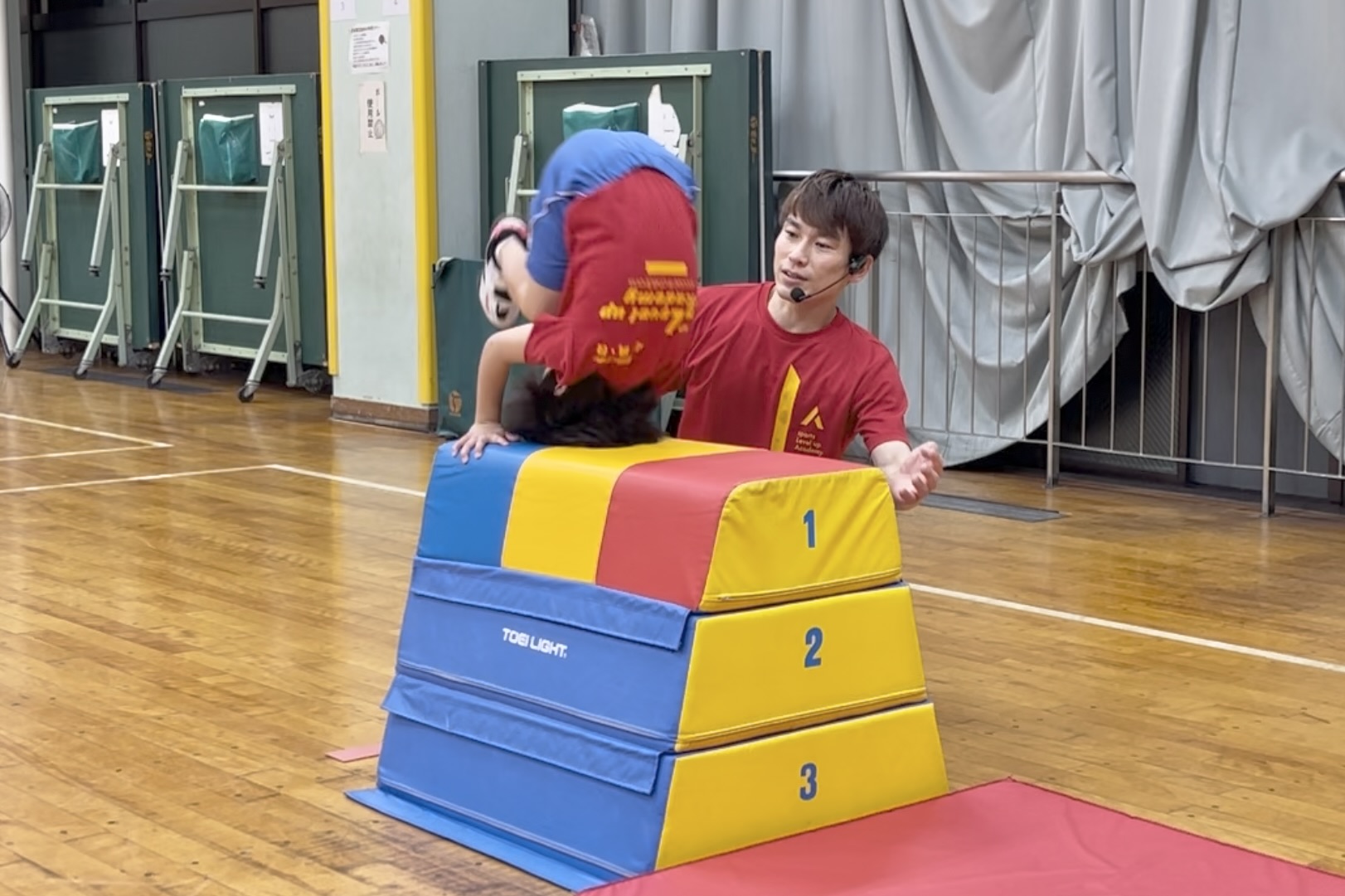 野々市教室にて、綺麗なフォームで跳び箱の「台上前転」をする幼児と、補助姿勢をとる大久保先生
